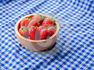 Strawberry in a wooden cup on blue and white checkered fabric texture