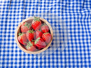 Strawberry in a wooden cup on blue and white checkered fabric texture