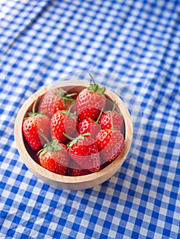 Strawberry in a wooden cup on blue and white checkered fabric texture