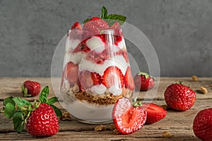 Strawberry yogurt parfait with granola, mint and fresh berries in a glass on rustic wooden table. delicious healthy food