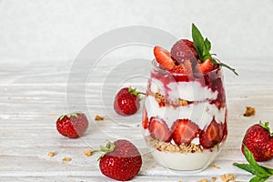 Strawberry yogurt parfait with granola, mint and fresh berries in a glass on white wooden table
