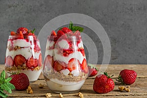 Strawberry yogurt parfait with granola, mint and fresh berries in glasses on rustic wooden table. healthy breakfast