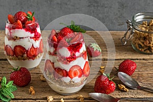 Strawberry yogurt parfait with granola, mint and fresh berries in glasses with spoons on rustic wooden table