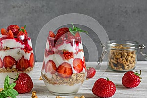 Strawberry yogurt parfait with granola, mint and fresh berries in glasses on white wooden table. healthy breakfast