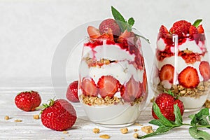 Strawberry yogurt parfait with granola, mint and fresh berries in glasses on white wooden table. healthy breakfast