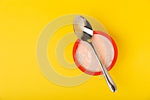 strawberry yogurt in a red plastic cup with a spoon on background.