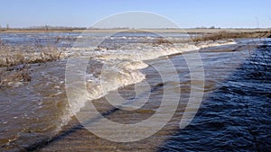 Stream of dirty, brown meltwater on a sunny spring day.