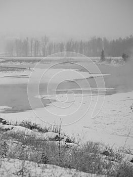 Stream flowing in frozen field on gloomy winter day, black and white