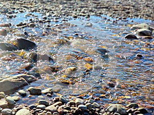 Stream flowing over stones, sun glare in the water.