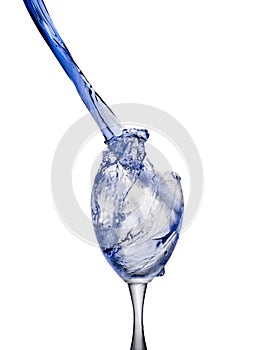 A stream of poured bright blue liquid splashes into a clear wine glass, on a clean white background.