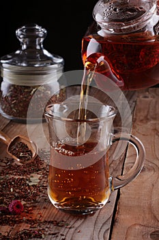 A stream of rooibos tea pouring from the teapot to a transparent glass cup