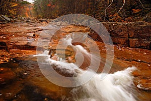 A stream rushes past stone banks and fall foliag