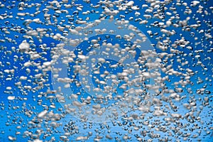 A stream of shiny air bubbles illuminated by light and shining on a blue background. Close up of light lit oxygen