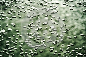 A stream of shiny air bubbles illuminated by light and shining on a dark background. Close up of light lit oxygen