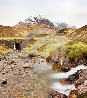 Stream and stony bridge in spring Higland mountains in Scotland. Snowy mountains in heavy clouds. photo