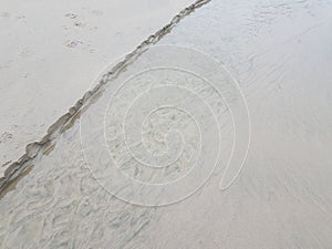 Stream of water at beach eroding sand and foot print