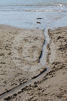 A stream of water flowing across a sandy beach