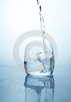 A stream of water flowing into a transparent glass cup with a splash of drops and drops. A jet of clean drinking spring water