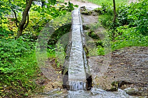 Stream of water flows in wooden gutter in the park