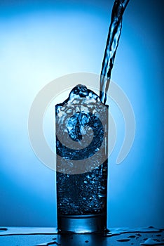 A stream of water pours into the glass close-up. Water spray, blue background