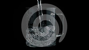 A stream of water pours into a transparent glass, beautiful splashes and glasses. Black background with illumination of