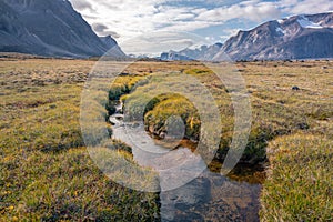 Stream winds through wild arctic landscape in Akshayuk Pass, Baffin Island, Canada. Moss valley floor and dramatic