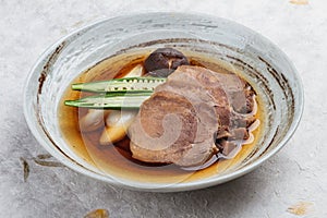 Streamed beef tounge gyutan served with shiitake, Japanese scallion and chilli with soup in rounded stone plate on washi.