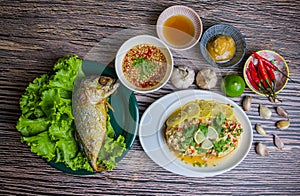 Streamed chicken meat with Thai lemon sauce and fried fish served on  plates on wooden table,look tasty and delicious.