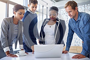 Streamlining their workflow. a group of coworkers working together on a laptop in an office.