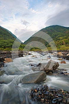 Streams and rocks between mountains with blue sky and green trees