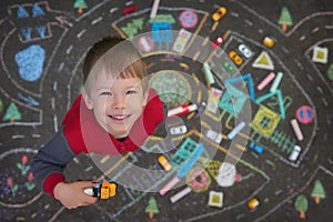 Streat portrait of the preschool boy playing cars in the chalk drawn city