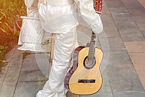 Street artist painted in white silver paint walking in city park. Living statue performer with guitar