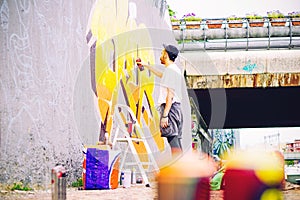 Street artist painting a colorful graffiti on a grey wall under bridge - Young graffiter writing and drawing murales