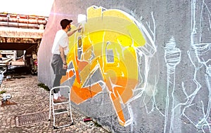 Street artist working on colored graffiti at public space wall - Modern art perform concept of urban guy painting live murales