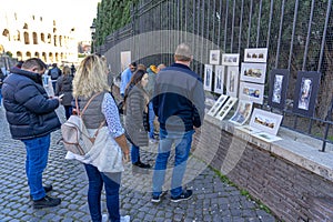street artists selling paintings and tourists watching.  between the coliseum and the entrance to the palatine hill, Rome, Italy