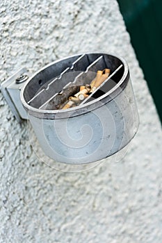 Metal ashtray on a wall full with cigarette old retro style not cleaned