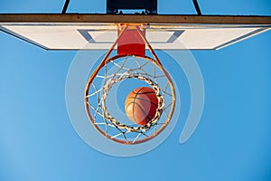 Street basketball ball falling into the hoop. Urban youth game. Close up of orange ball above the hoop net. Concept of success,