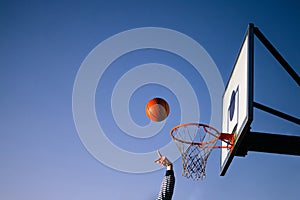 Street basketball ball player throwing ball into the hoop. Close up of hand, orange ball above the hoop net with blue sky in the