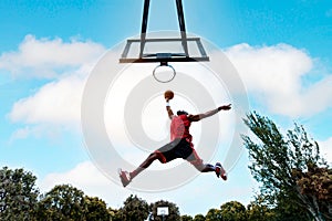 Street basketball player making a powerful slam dunk on the court - Athletic male training outdoor at sunset