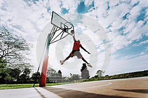 Street basketball player making a powerful slam dunk on the court - Athletic male training outdoor at sunset