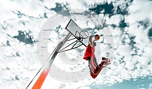 Street basketball player making a slam dunk on the court - Athletic male training outdoor on a cloudy sky background