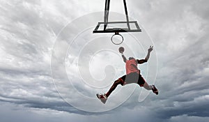 Street basketball player making a slam dunk on the court - Athletic male training outdoor on a cloudy sky background