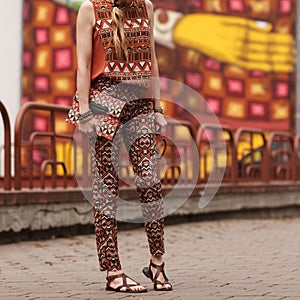 Street, bright style. A young woman in the costume with ornament,black jacket, clutch, sandals, sunglasses. Details