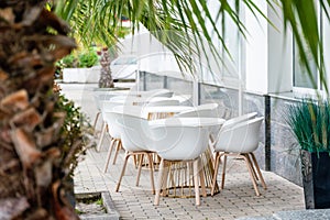 Street cafe with white chairs, green foliage around. Without people, tourism, travel.