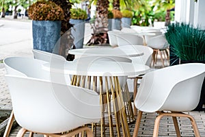 Street cafe with white chairs, green foliage around. Without people, tourism, travel.