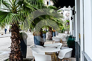 Street cafe with white chairs, green foliage around. Without people, tourism, travel.
