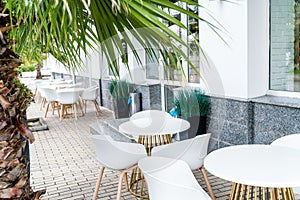 Street cafe with white chairs, green foliage around. Without people, tourism, travel.