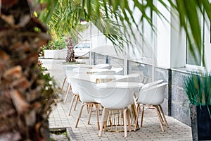 Street cafe with white chairs, green foliage around. Without people, tourism, travel.