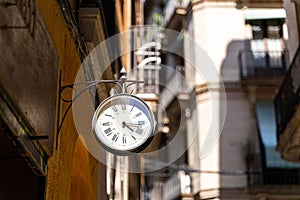 Street clock with arrows on wall with background of buildings in Barcelona