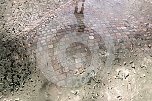 Street with cobble stones and puddle after rain seen through wet window pane